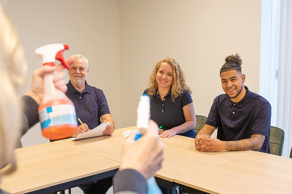 Schoonmakers kijken vrolijk naar een instructie over schoonmaakmiddelen