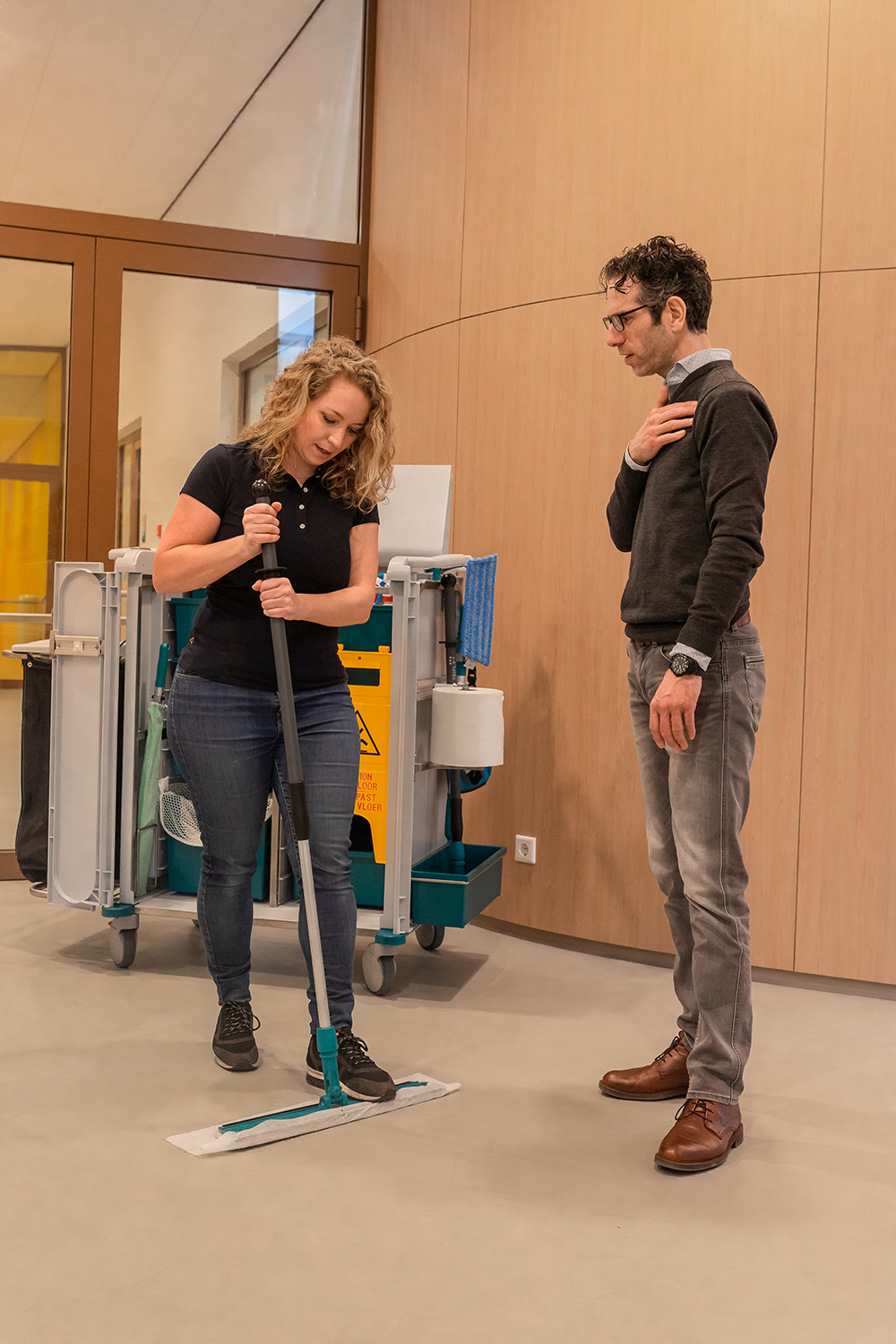 Instructeur begeleidt schoonmaker bij stofwissen