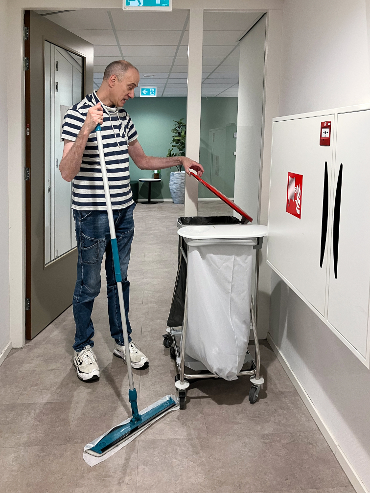 Medewerker Amarant met stofwisser bij vuilnistrolley
